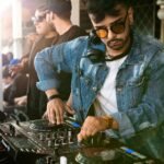 DJ mixing music at vibrant daytime event with crowd enjoying the performance.